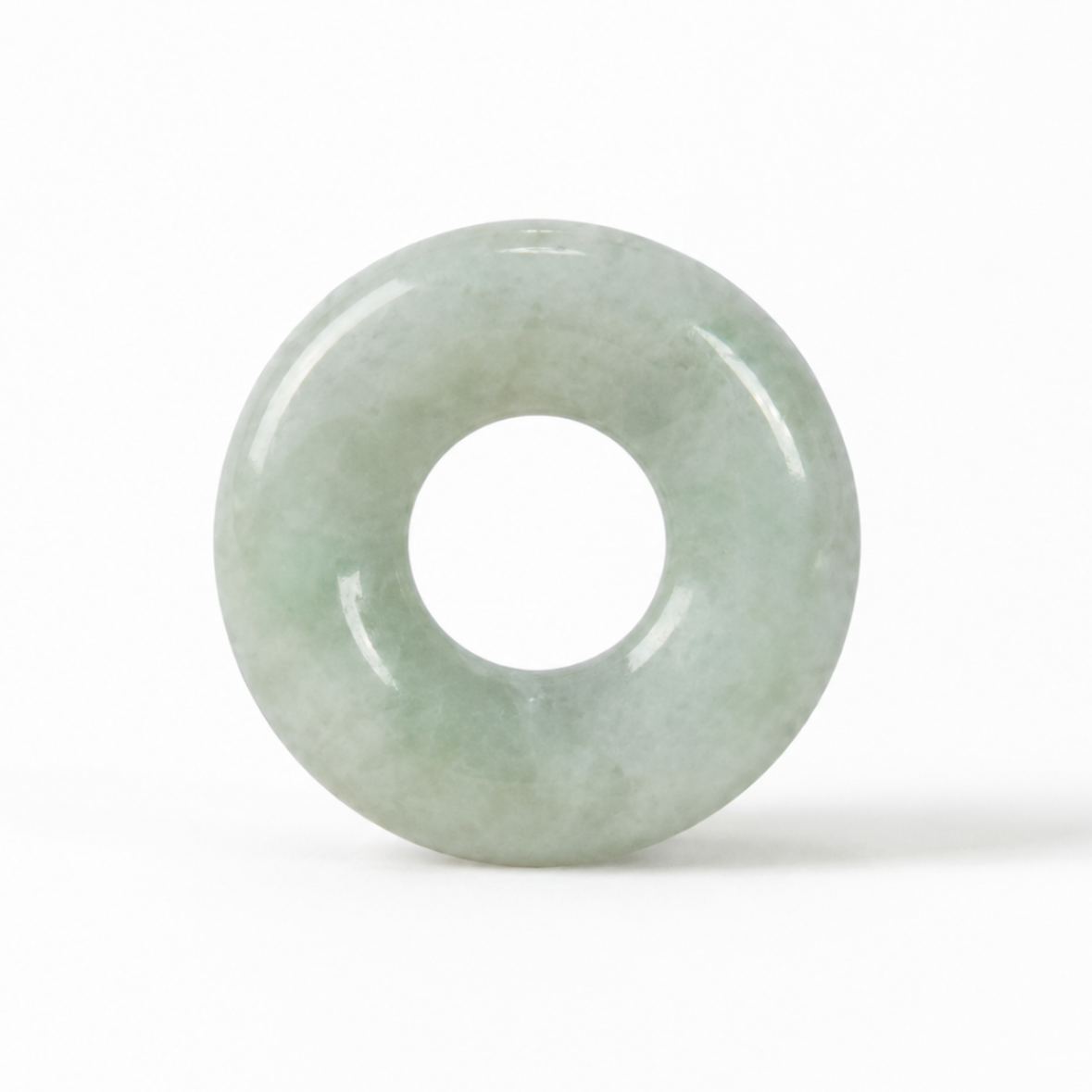 A light green jadeite donut-shaped pendant or amulet with a smooth, polished surface, centered on a clean white background.