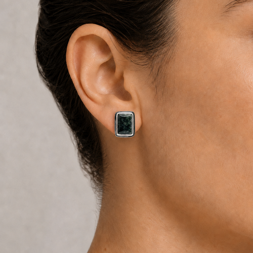 Close-up of an ear wearing a square-shaped earring with a dark jade gemstone on a neutral background