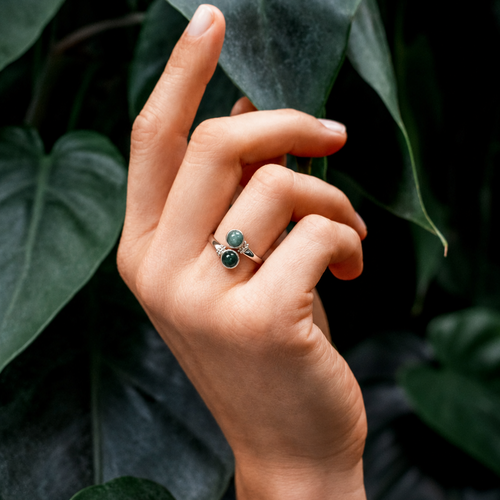 Hand wearing a jade ring against a leafy background