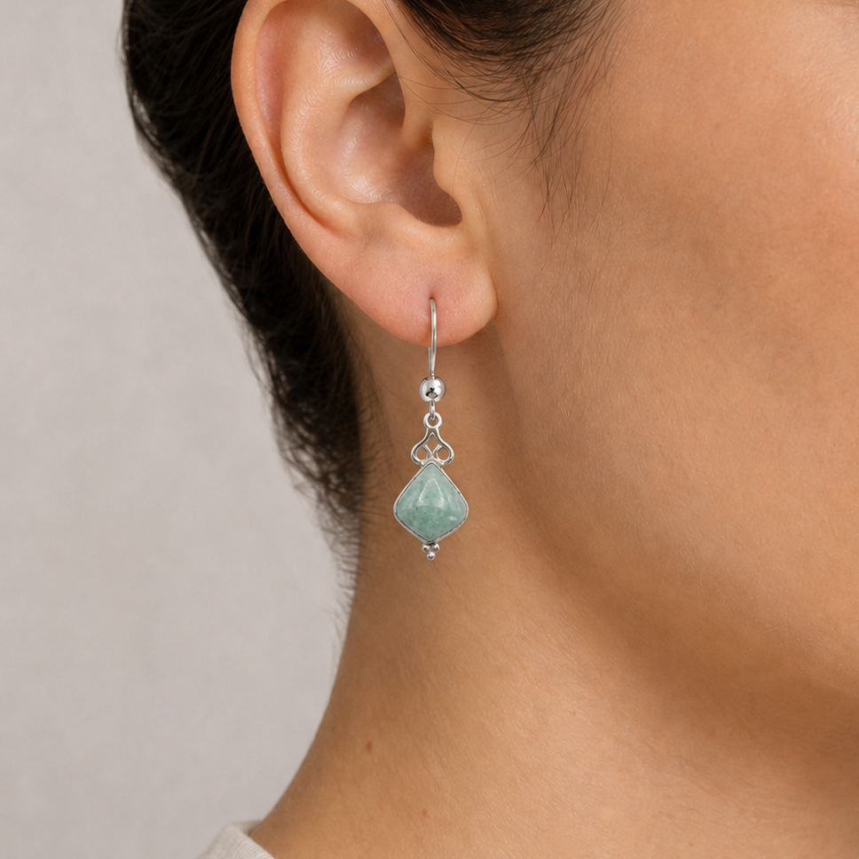 Close-up of a woman wearing a light green jade earring with a neutral background
