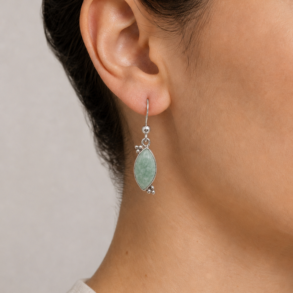 Close-up of a person wearing a jade earring with sterling silver on a neutral background