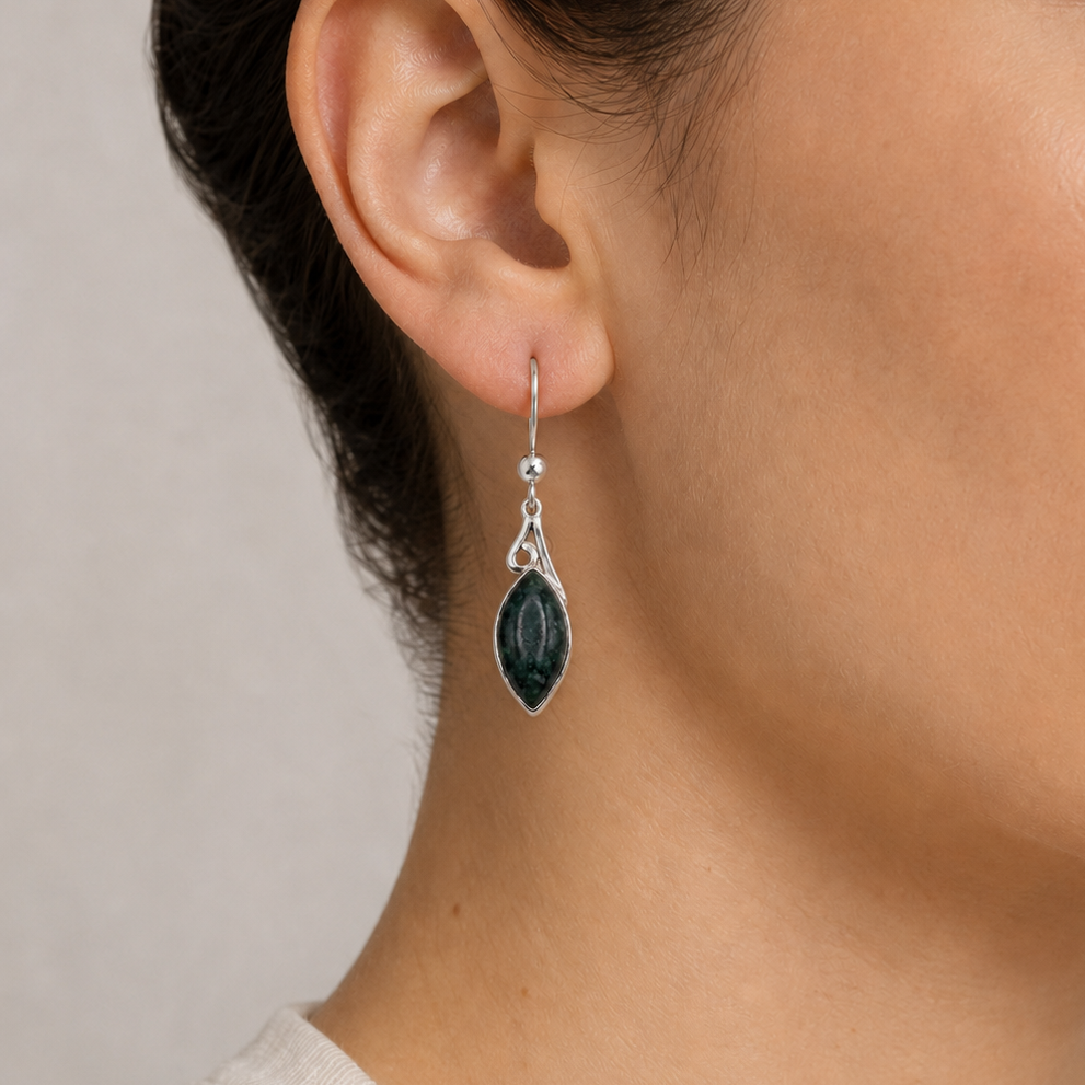 Close-up of an ear wearing a silver earring with a jade gemstone on a neutral background