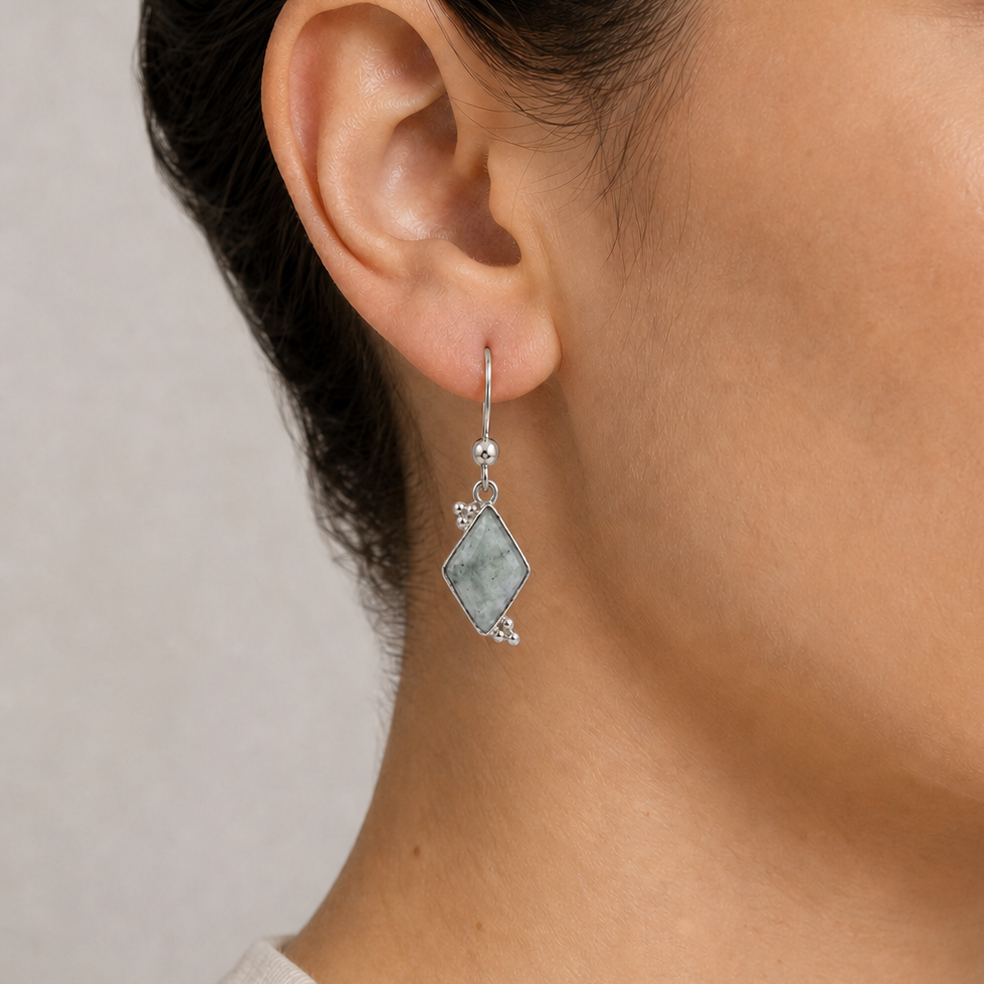 Close-up of an ear wearing a silver earring with a jadeite jade stone on a neutral background