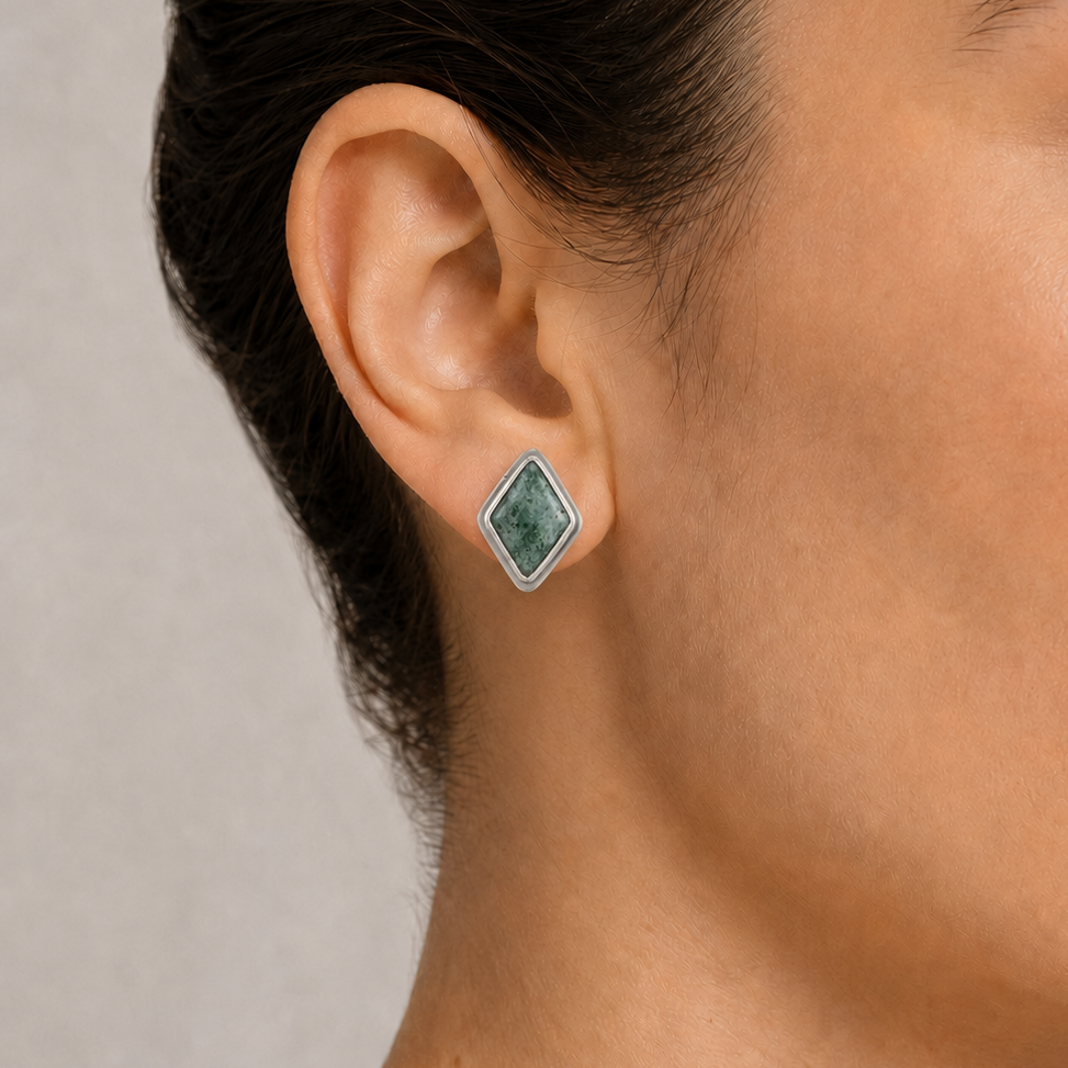Close-up of a woman wearing a silver earring with a jade gemstone on a neutral background
