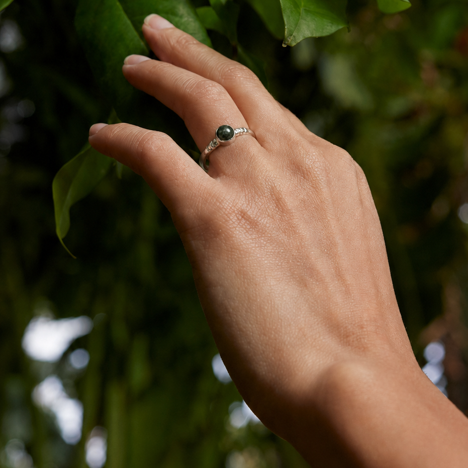 Hand with a jade ring touching green leaves against a blurred natural background