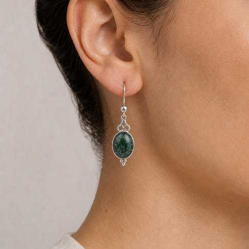 Close-up of an ear wearing a green jaguar jade earring with silver detailing on a neutral background