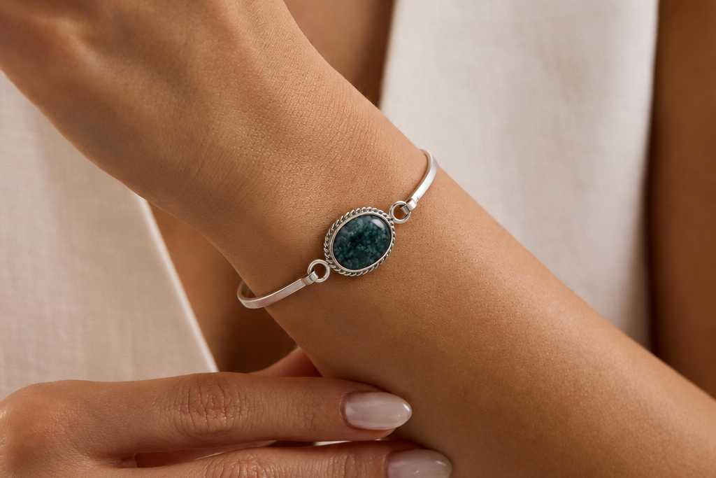 Close-up of a wrist wearing a silver bracelet with a jade gemstone, against a neutral background.