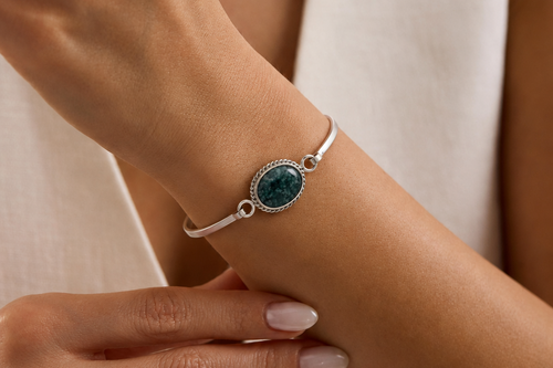 Close-up of a wrist wearing a silver bracelet with a jade gemstone, against a neutral background.