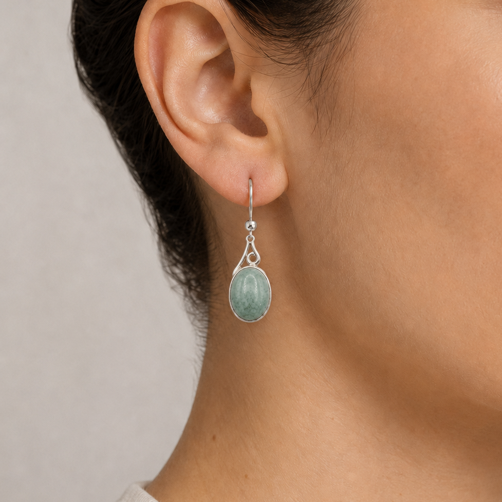 Close-up of a person wearing a silver earring with a green jade gemstone on a neutral background