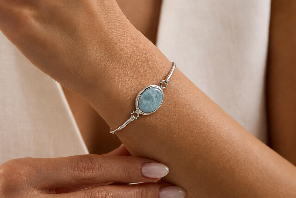 Close-up of a wrist wearing a silver bracelet with a blue jade gemstone, against a neutral background.