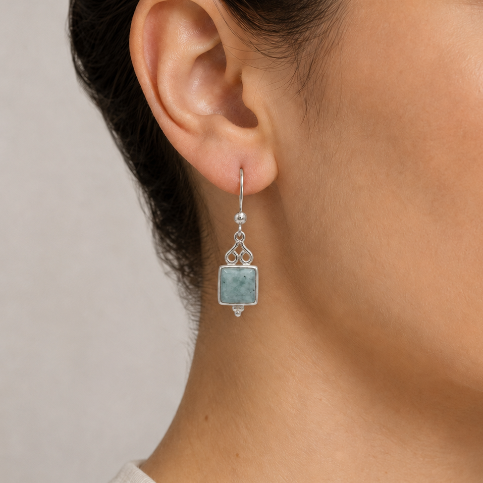 Close-up of a woman wearing a silver earring with a jade gemstone on a neutral background